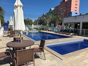 Una piscina con sillones de descanso y sombrillas, rodeada de edificios.