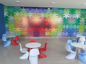 Una habitación con pared de diseño tipo puzzle, mesas redondas y sillas de colores.