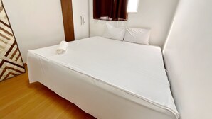 Una cama bien hecha en una habitación con suelo de madera, un armario y una ventana con cortinas.