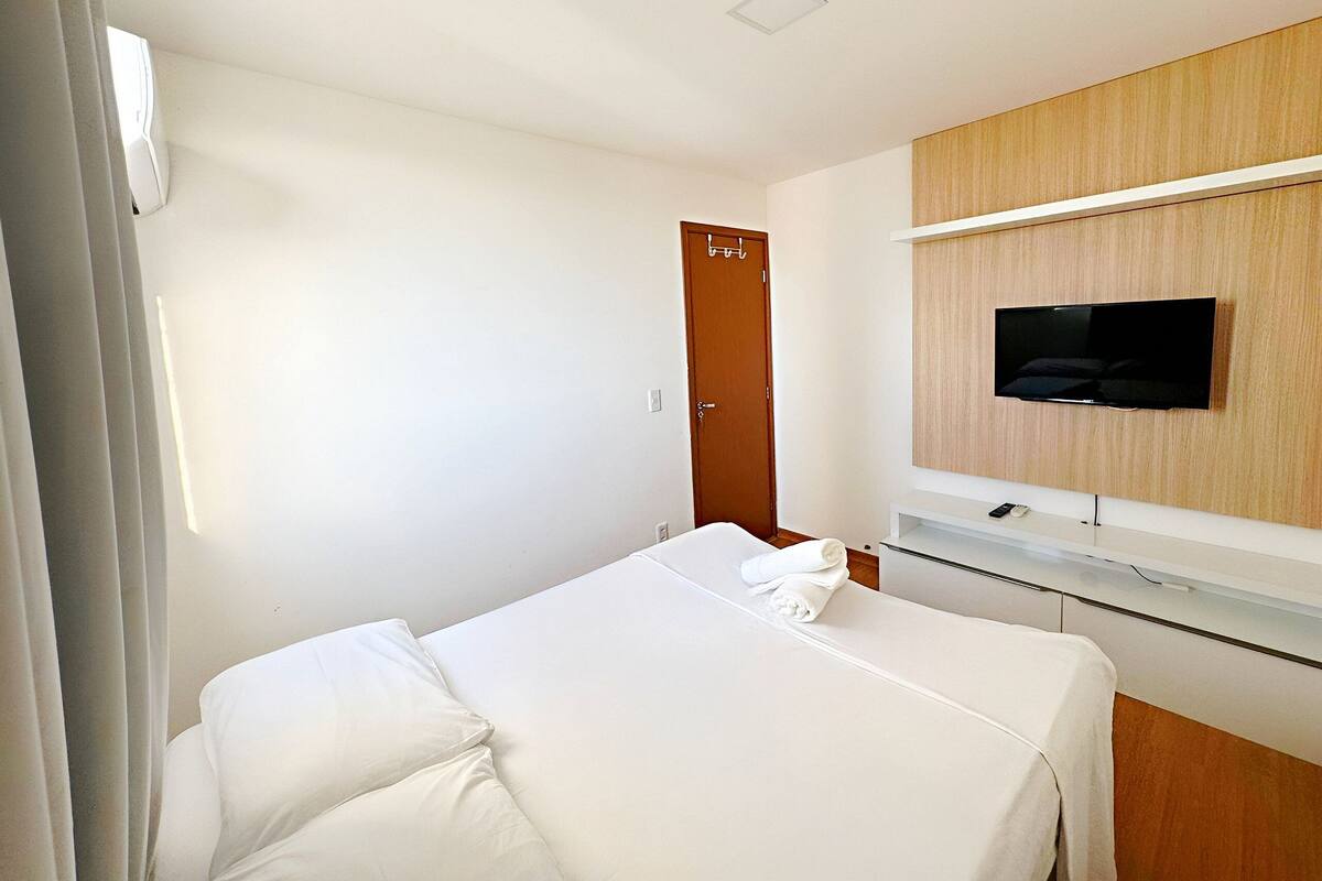 Une chambre d’hôtel avec un lit, un téléviseur fixé au mur, une porte en bois et un mur blanc.