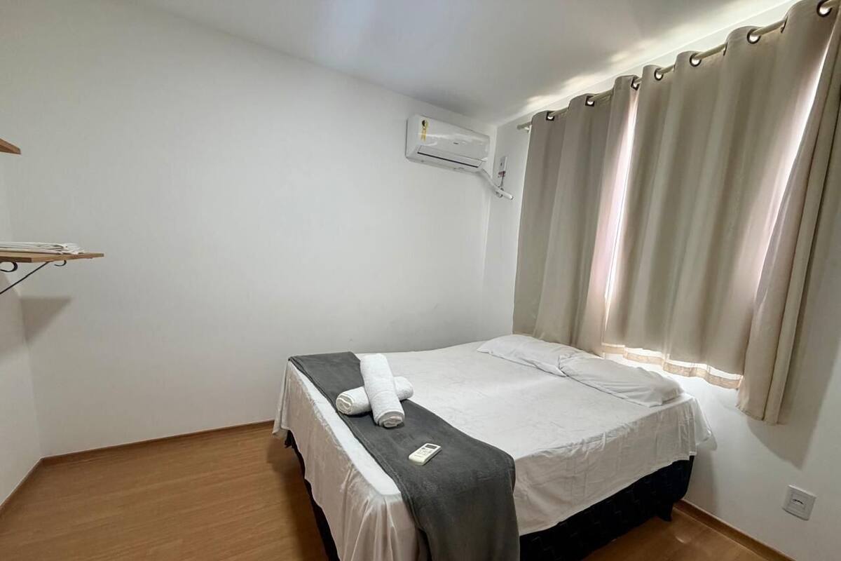 Un lit simple avec une couverture grise, un oreiller blanc et une serviette enroulée sur le côté. Il y a une petite table sur laquelle est posée une serviette blanche pliée.