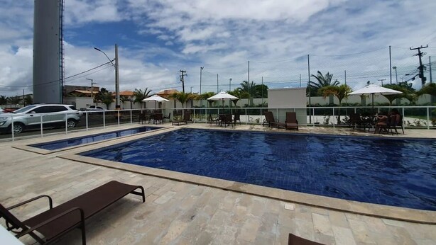 Piscina con sillones de descanso y sombrillas, rodeada por una valla y palmeras.