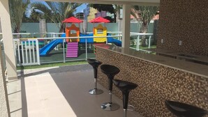 Un patio con un parque infantil, una barra con taburetes y piso de baldosas.
