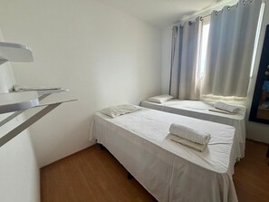 Una habitación con dos camas individuales, un escritorio pequeño y una ventana con cortinas.