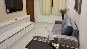 Una sala de estar moderna con un televisor de pantalla plana, un sofá gris, una mesa de comedor con una orquídea decorativa y una planta en maceta.