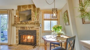 A cozy room with a stone fireplace, a dining table with chairs, and a large window with blinds. - 1 Mi to Sugar Mountain! Cozy Lodge-Style Condo (Banner Elk)