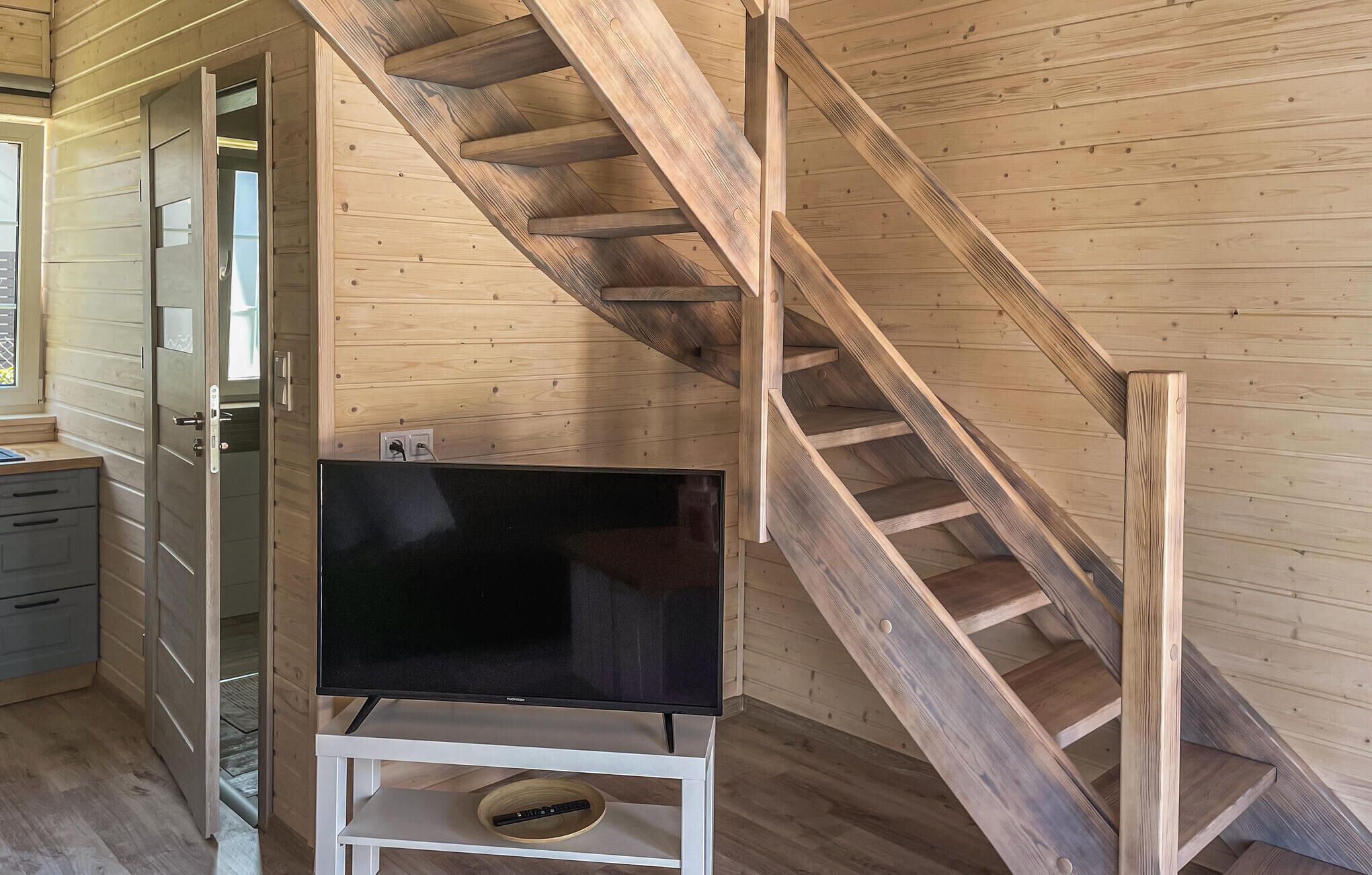 A wooden interior with a staircase, a television on a stand, and a door leading to another room.