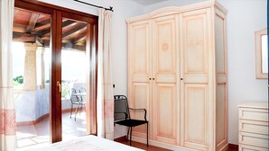 Une chambre dotée d’une grande armoire, d’un lit, d’une chaise et donnant sur un patio extérieur avec des chaises et une table.