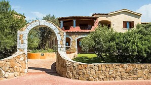 Une villa de style méditerranéen avec une entrée en arc de pierre, de nombreux balcons et une végétation luxuriante.