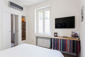 A bedroom with a bed, a TV mounted on the wall, a radiator, a window, and a door leading to another room. - Green Shot - Garibaldi Area (Milano)
