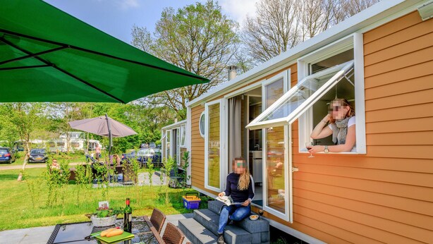A mobile home with a patio area, outdoor seating, and a window with a view of the surrounding area. - Stunning (sta)caravan in Hoogersmilde (Hoogersmilde)