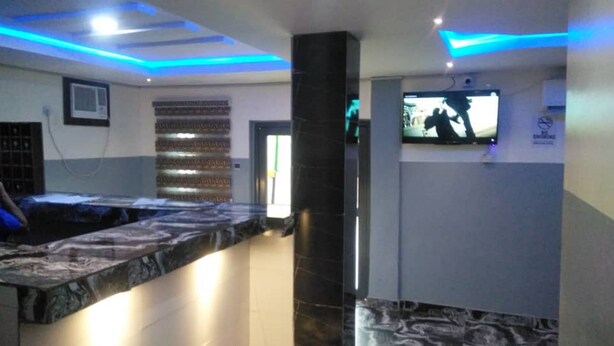 Un área de recepción con mostrador de mármol, televisor montado en la pared y un pilar con base negra.