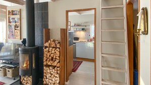A cozy living room with a fireplace, a wooden log stack, and a kitchen area visible through an open door. - Lovely home in Taberg with kitchen (Taberg)