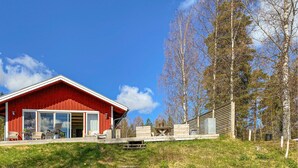 A red wooden cabin with a glass door entrance, a small patio with outdoor furniture, and a wooden fence. - Lovely home in Taberg with kitchen (Taberg)