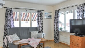 A living room with a grey sofa, a wooden TV stand, and a window with curtains.