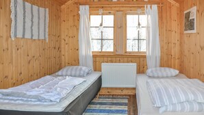 A wooden cabin with two single beds, a window with curtains, and a radiator.