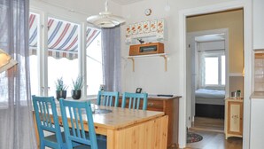 A dining area with a wooden table and blue chairs, a radio on a shelf, and a bed in the adjacent room.
