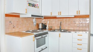 A compact kitchen with white cabinets, a stove, a sink, and a spice rack.