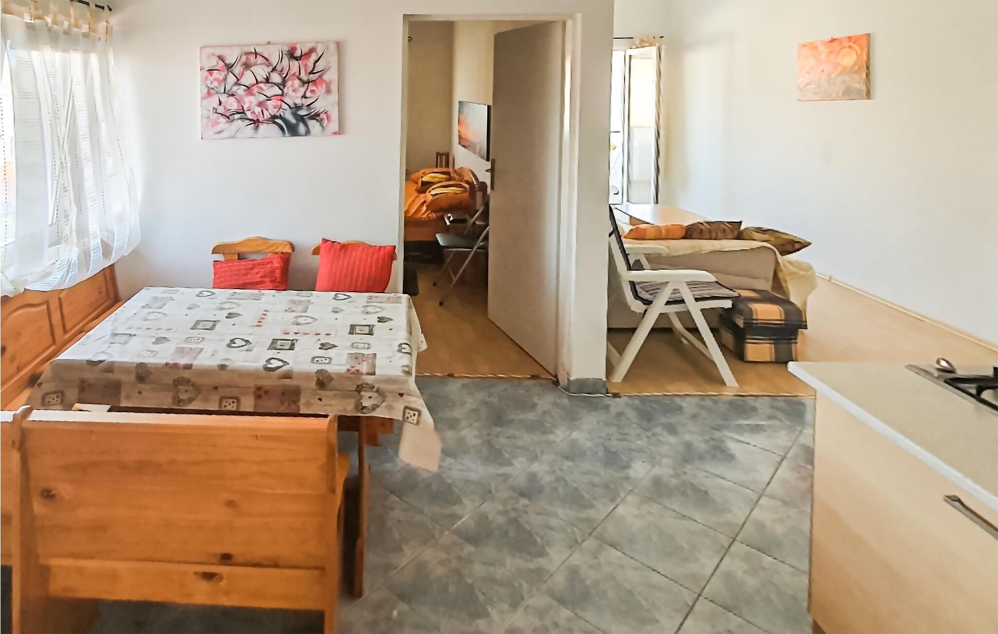 A room with a wooden dining table, a bed with a patterned bedspread, and a small kitchenette.