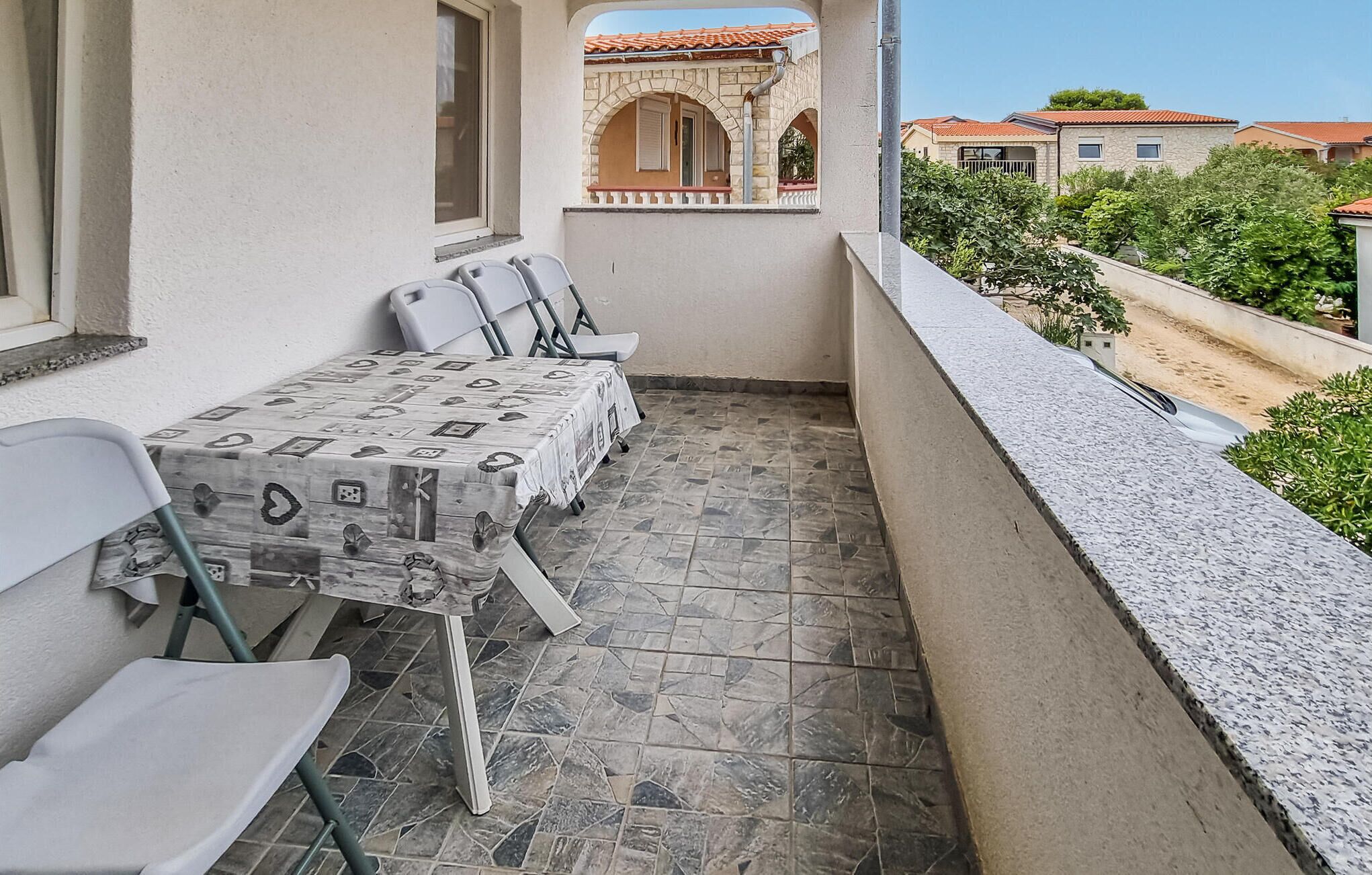 Ein Balkon mit Tisch und Stühlen, ein Fliesenboden und Blick auf angrenzende Gebäude.