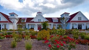 A large white building with red roofs and multiple windows, surrounded by a garden with various plants and flowers.