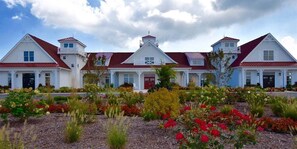 A large white building with red roofs and multiple windows, surrounded by a garden with various plants and flowers.