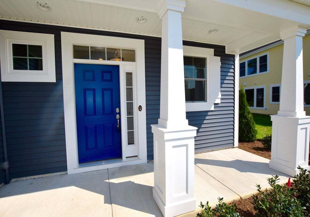 A residential house with a blue front door, white columns, and a covered porch.