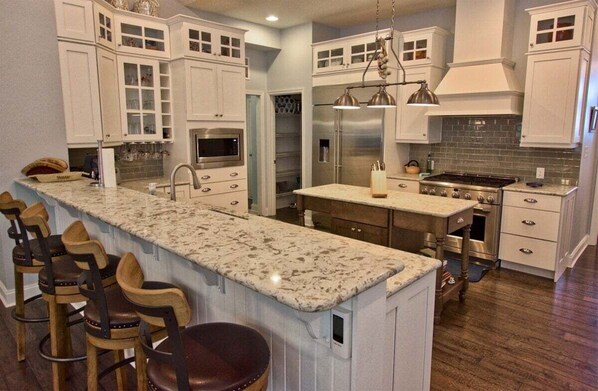 A kitchen with white cabinets, a granite countertop, stainless steel appliances, and a bar area with stools.