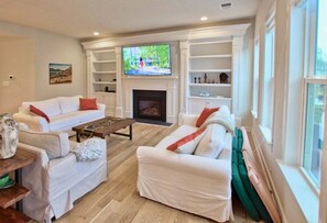 A living room with white sofas, a fireplace, a TV, and a bookshelf. - Coastal Club * 4BR Luxury House (Lewes)