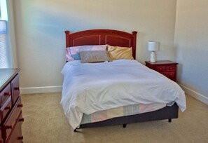 A bedroom with a wooden bed, a bedside table with a lamp, and a dresser. - Coastal Club * 4BR Luxury House (Lewes)