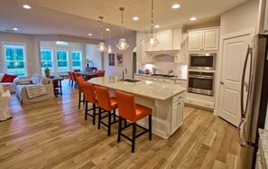 A spacious kitchen with a large island, modern appliances, and a dining area with orange chairs.