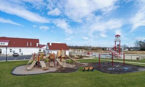A playground with slides and climbing structures, a red and white tower, and a building with a red roof in the background.
