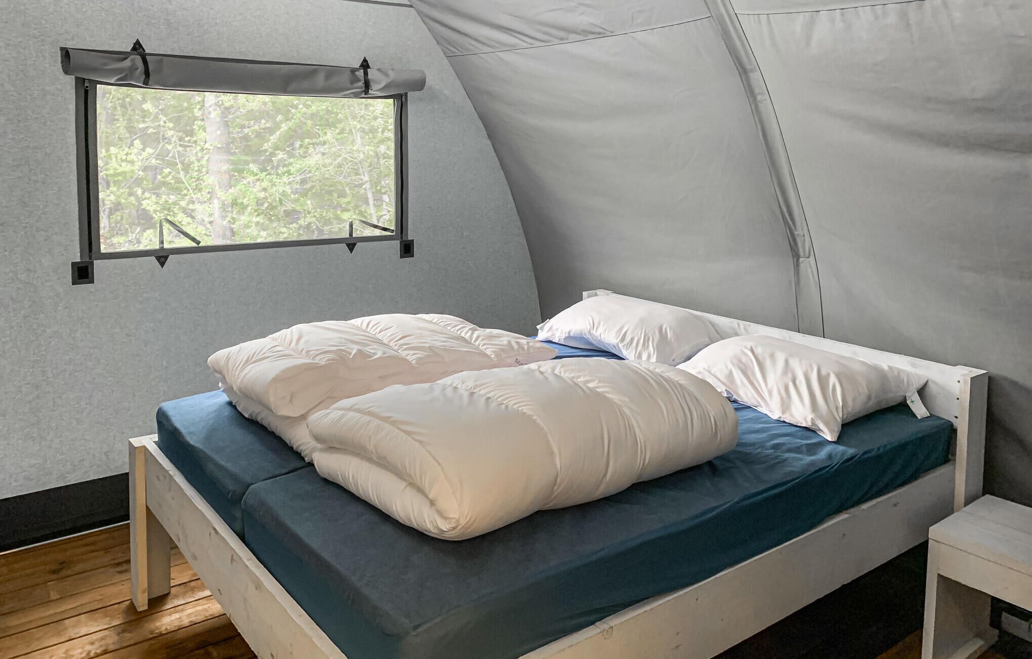 Uma cama de solteiro com roupa de cama branca em um quarto tipo tenda com janela.