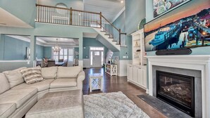 A spacious living room with a large sectional sofa, a fireplace, and a staircase leading to an upper level.