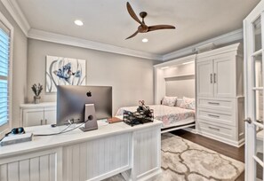 Ein Schlafzimmer mit Bett, Schreibtisch mit Computer, Deckenventilator und Kleiderschrank.
