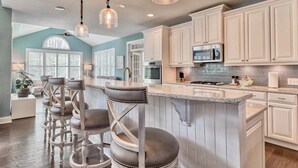 A kitchen with white cabinets, a central island with bar stools, and pendant lighting.