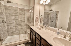 Un bagno moderno con doccia a vetro, due lavabi e uno specchio grande.