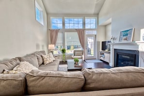 A living room with a sofa, a coffee table, a fireplace, and large windows.