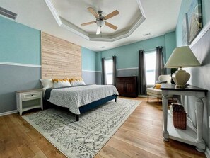 A bedroom with a bed, nightstands, a desk, a chair, a ceiling fan, and a fireplace.