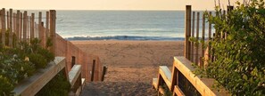 A wooden pathway leading to a beach with a fence on both sides.