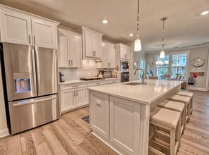 A modern kitchen with white cabinetry, stainless steel appliances, a central island with stools, and pendant lighting.
