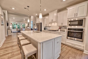 A spacious kitchen with white cabinetry, a large island with stools, stainless steel appliances, and pendant lighting.