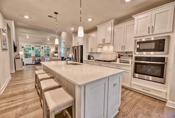A spacious kitchen with white cabinetry, a large island with stools, stainless steel appliances, and pendant lighting.