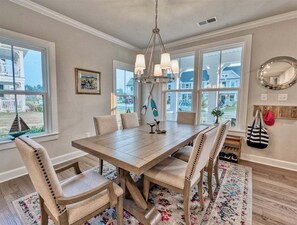 A dining room with a wooden table, four chairs, a chandelier, and large windows.