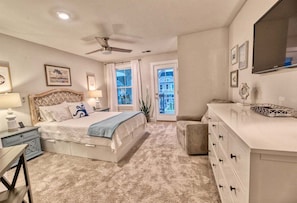 A bedroom with a bed, bedside tables, a dresser, a ceiling fan, and a view through a door.