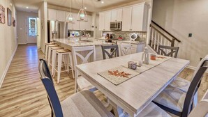 Una cocina moderna con armarios blancos, una isla central y un comedor con mesa y sillas.