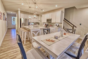 Une cuisine moderne avec des meubles blancs, un Ăźlot central et un coin repas comprenant une table et des chaises.