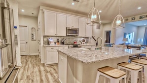 Una cocina moderna con armarios blancos, encimera de granito y refrigerador de acero inoxidable.