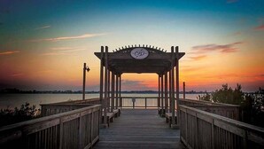 Un muelle de madera que conduce a un pabellón con un emblema circular, con vistas a un cuerpo de agua al atardecer.