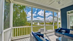 A covered porch with wicker furniture and a view of a lake and houses.